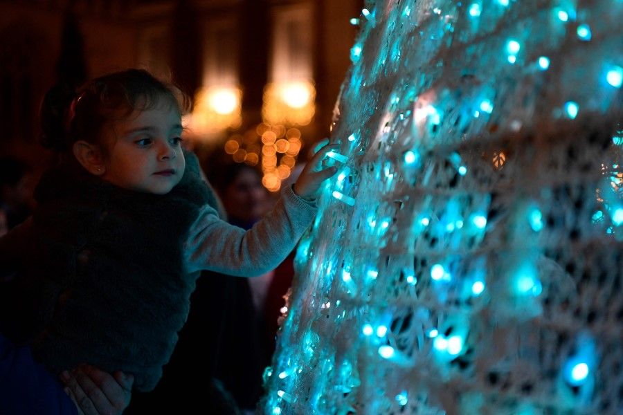 A little girl touches the lights of a Christmas tree in Seville on 17 December 2022. (Cristina Quicler/AFP)