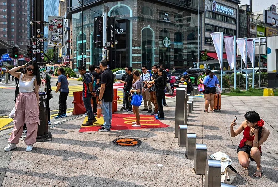 A woman poses for pictures on the sidewalk in Kuala Lumpur on 24 April 2024. (Mohd Rasfan/AFP)
