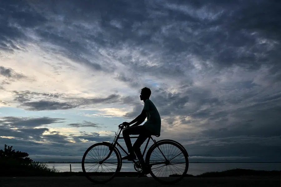 A man paddles his bicycle down an embankment along the banks of river Brahmaputra as dark clouds loom over Dibrughar in India’s northeastern state of Assam on 23 June 2025.