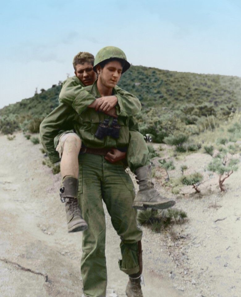 A soldier carrying an injured comrade as the US army pushes towards North Korea, September 1950.