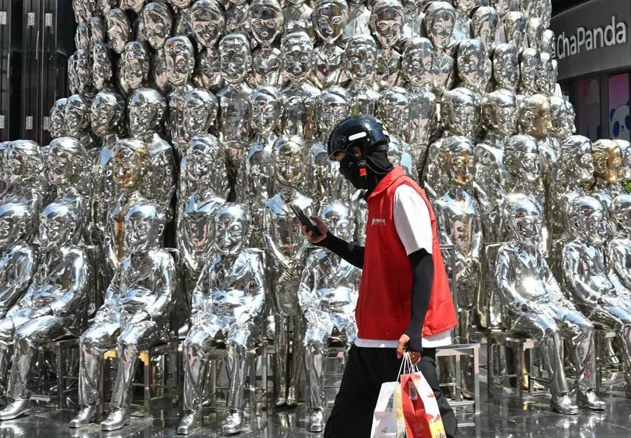 A food delivery worker walks past an art installation at a shopping mall in Beijing on 24 August 2026.