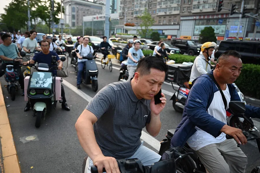 A man makes a phone call while waiting on his e-bike at an intersection in Beijing on 9 July 2024. (Greg Baker/AFP)