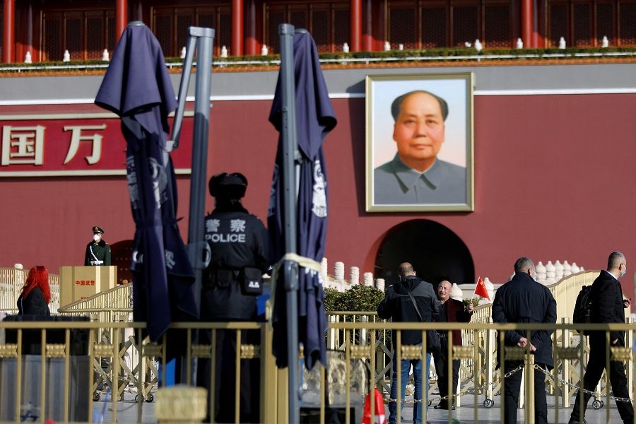 A man poses under a portrait of late Chinese Chairman Mao Zedong near police and paramilitary officers standing guard at the Tiananmen Gate, in Beijing, China, 3 March 2023. (Florence Lo/Reuters)