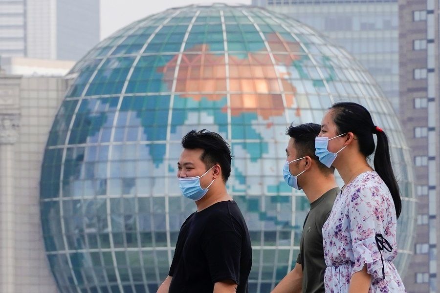 People wearing protective face masks walk along The Bund in front of the Lujiazui financial district of Pudong, in Shanghai, China, 25 August 2021. (Aly Song/Reuters)
