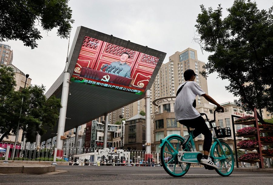 A man cycles in front of a screen showing Chinese President Xi Jinping speaking during a celebration marking the 100th founding anniversary of the Communist Party of China, in Beijing, China, 1 July 2021. (Thomas Peter/Reuters)