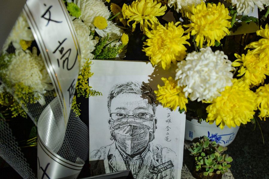 This photo taken on 7 February 2020 shows a photo of the late ophthalmologist Li Wenliang with flower bouquets at the Houhu Branch of Wuhan Central Hospital. (STR/AFP)