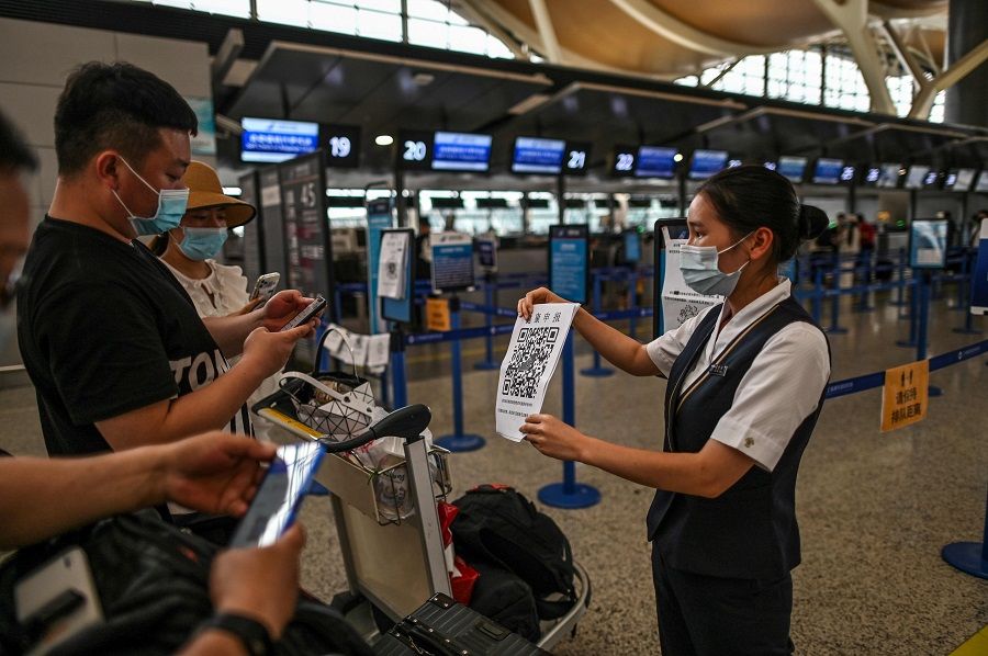 Passengers wearing face masks check their health code with a sheet held by an airport staff (right) before the counter area in Pudong International Airport in Shanghai, on 11 June 2020. (Hector Retamal/AFP)