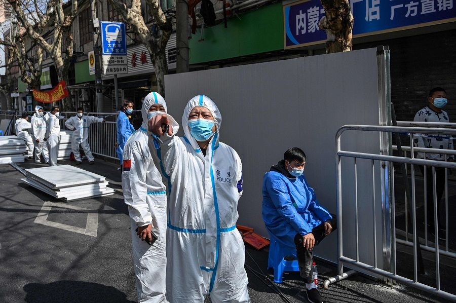 A policeman (centre) wearing protective clothing reacts in an area where barriers are being placed to close off streets around a locked down neighbourhood after the detection of new Covid-19 cases in Shanghai, China, on 15 March 2022. (Hector Retamal/AFP)