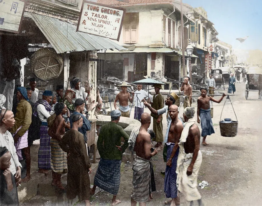 Indians with sarongs wrapped around their waists and hawkers balancing their wares on poles stand outside the tailor shops at the junction of Cross Street and South Bridge Road in the late 19th century. This is a vivid portrait of those who were at the lowest rung of society then.