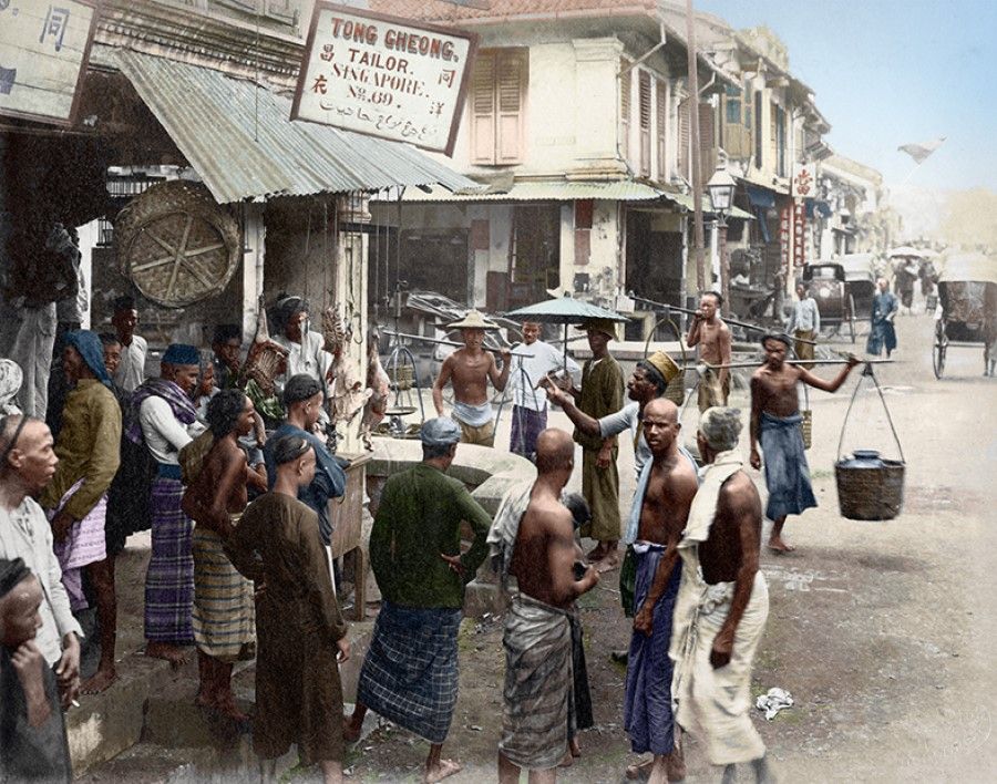 Indians with sarongs wrapped around their waists and hawkers balancing their wares on poles stand outside the tailor shops at the juncture of Cross Street and South Bridge Road in the late 19th century. This is a vivid portrait of those who were at the lowest rung of society then.