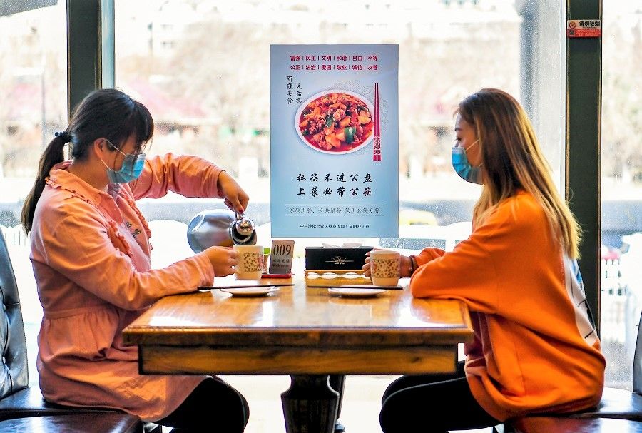 In this photo taken on 3 April, a poster encouraging people to use serving chopsticks and sit apart is seen as two diners wait for their food to be served in a restaurant in Saybag District, Ürümqi, Xinjiang, China. (CNS)