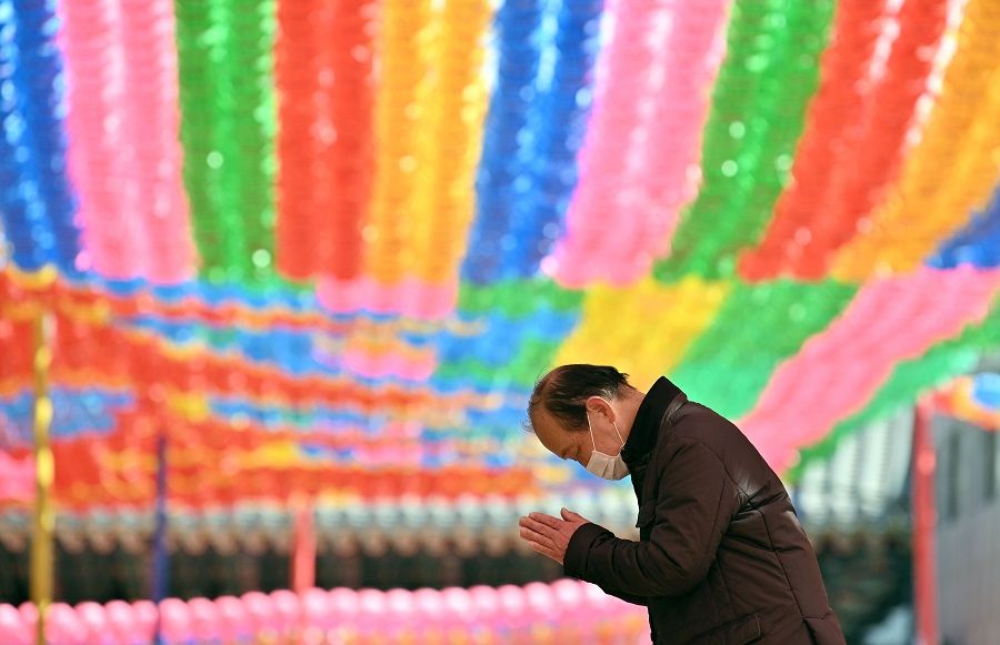 A Buddhist follower wearing a face mask prays under rows of lotus lanterns ahead of Buddha's birthday at Jogyesa Temple in Seoul on 23 March 2020. (Jung Yeon-je/AFP)