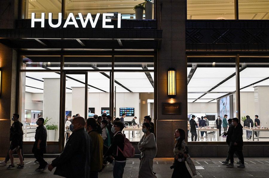 People walk next to a Huawei shop along a pedestrian street surrounded by shops and shopping malls in Shanghai, on 12 October 2022. (Hector Rtamal/AFP)