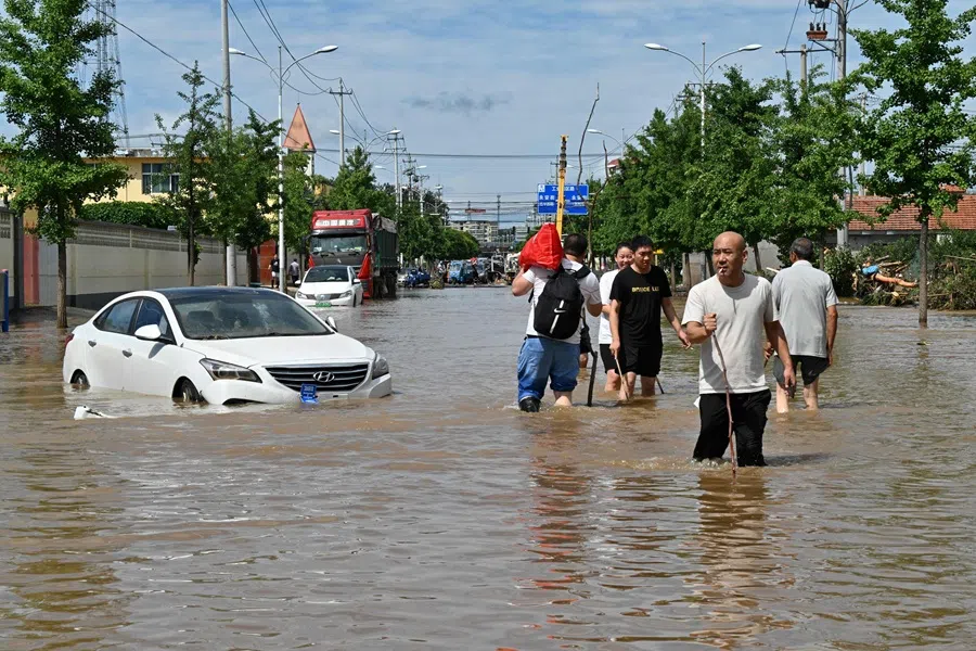 People wade in a flooded street in Miyun district, Beijing, China, on 29 July 2025. (Adek Berry/AFP)