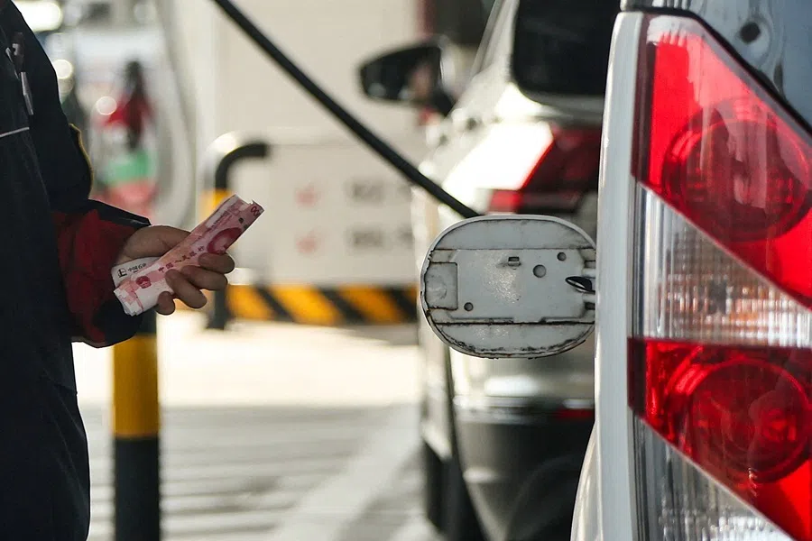 An employee holds Chinese Yuan notes next to an open cap of a car's fuel tank at a gas station ahead of an announced fuel price hike, amid the US-Israeli conflict with Iran, in Beijing, China, on 22 March 2026.