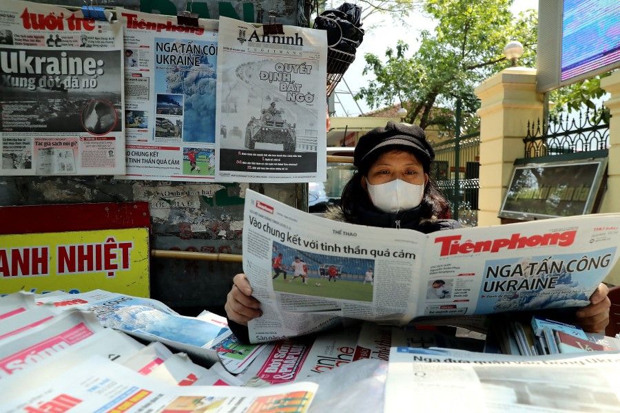 A woman reads a Vietnamese newspaper featuring front page coverage of the Russian invasion of Ukraine at her stall in Hanoi on 25 February 2022. (Nam Nguyen/AFP)