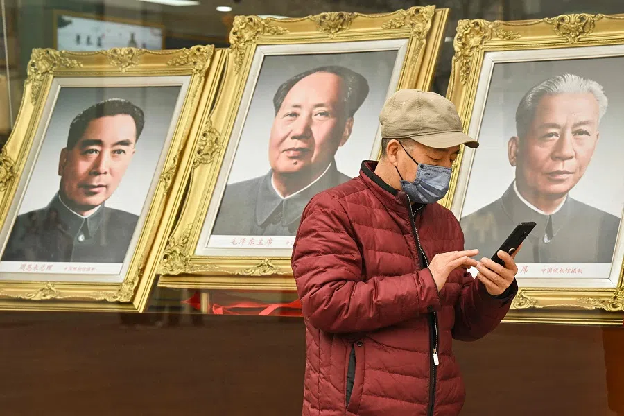 2025年3月11日，北京王府井商业街，一名男子走过一家照相馆时，一边查看手机，这家照相馆里挂满了已故中国共产党领导人毛泽东（中）、中国前总理周恩来（左）和中国前国家主席刘少奇的照片。（Adek Berry/法新社）