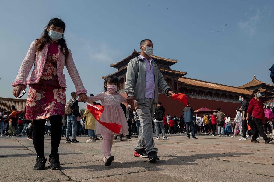 A family wearing face masks walks outside the Forbidden City (back) on 1 October 2020. (Nicolas Asfouri/AFP)