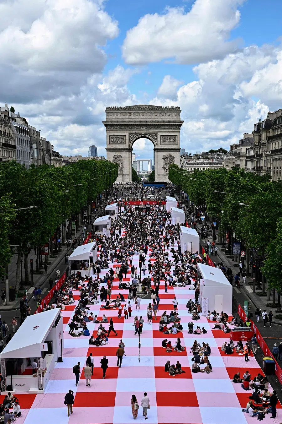 People take part in a giant open-air picnic on the Champs-Elysees avenue in Paris on 26 May 2024. Around 4,000 people were selected to have lunch on a 216-meter-long red-and-white chequered rug, the “world’s largest tablecloth”. (Julien de Rosa/AFP)