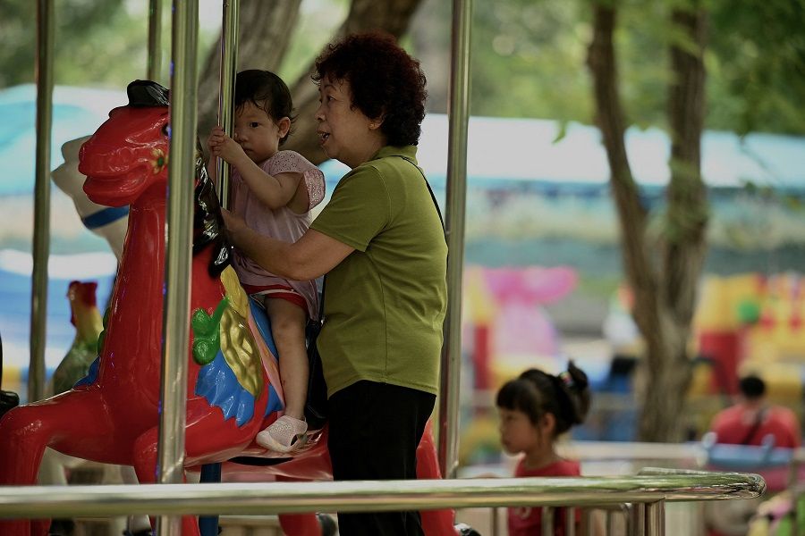 A woman tends to a child riding a merry-go-round at a park in Beijing, China, on 2 August 2022. (Noel Celis/AFP)