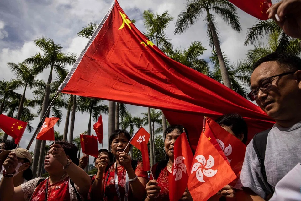 People wave the flags of Hong Kong and China on the Tsim Sha Tsui waterfront promenade in Hong Kong on 1 July 2023. (Isaac Lawrence/AFP)