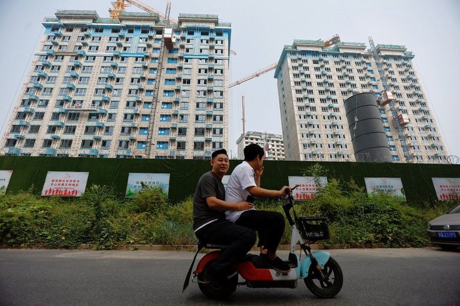 People ride on a scooter past residential buildings under construction in Beijing, China, on 6 September 2023. (Tingshu Wang/Reuters)