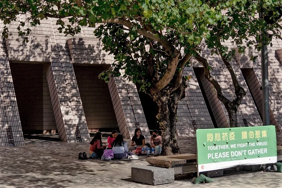 People enjoy a picnic near signage discouraging large gatherings amid the pandemic in Hong Kong's Tsim Sha Tsui area on 27 November 2021. (Bertha Wang/AFP)