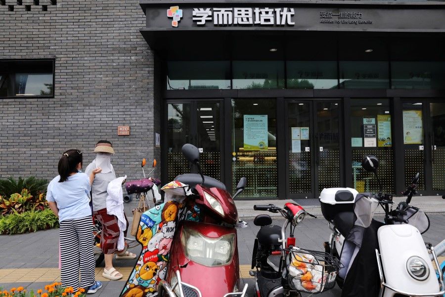 An adult and a girl is seen in front of a Xueersi outlet, a private educational services provider owned by TAL Education Group, in Beijing, China, 26 July 2021. (Tingshu Wang/Reuters)