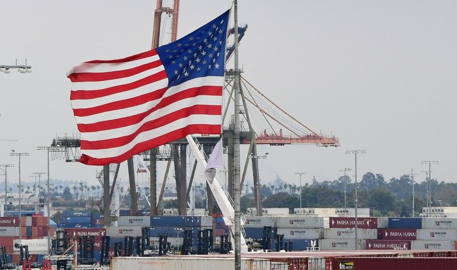 In this file photo the US flag flies in the foreground as containers are seen at the Port of Los Angeles on 18 June 2019 in San Pedro, California. Spending by American consumers and record-high imports as the global economy reopened drove the US trade gap to a new all-time high in March, the Commerce Department reported on 4 May 2021. The trade deficit rose 5.6% to US$74.4 billion, the highest ever recorded and mostly attributable to trade with China. (Frederic J. Brown/AFP)