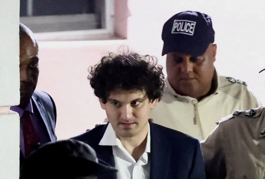Sam Bankman-Fried, who founded and led FTX until a liquidity crunch forced the cryptocurrency exchange to declare bankruptcy, is escorted out of the Magistrate Court building after his arrest in Nassau, Bahamas, 13 December 2022. (Dante Carrer/Reuters)
