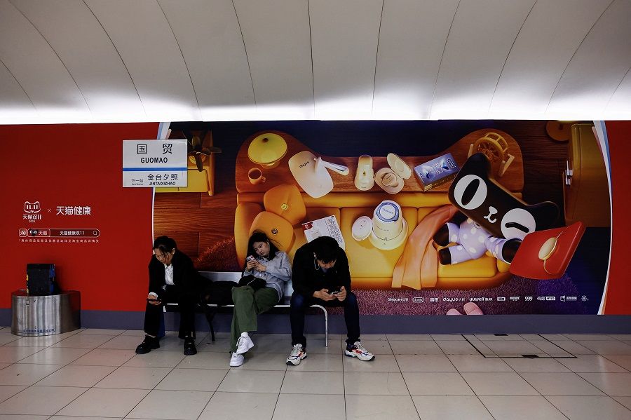 People sit near an advertisement promoting the Singles' Day shopping festival, at a subway station in Beijing, China, on 26 October 2023. (Tingshu Wang/Reuters)