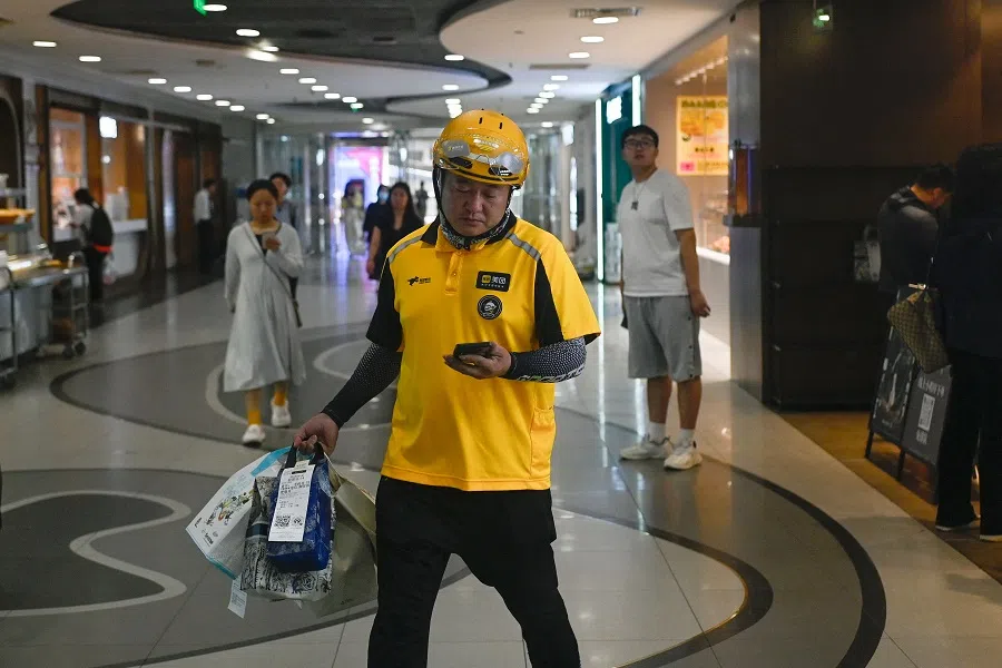 A food delivery worker looks at his mobile phone while carrying items to be delivered at a mall in Beijing, China, on 10 July 2024. (Wang Zhao/AFP)