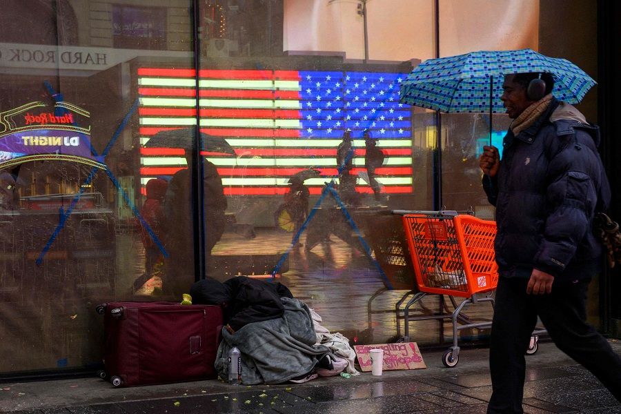 A person with an umbrella walks past a homeless person at Times Square during a rainy day on 19 January 2023 in New York City, US. (Angela Weiss/AFP)