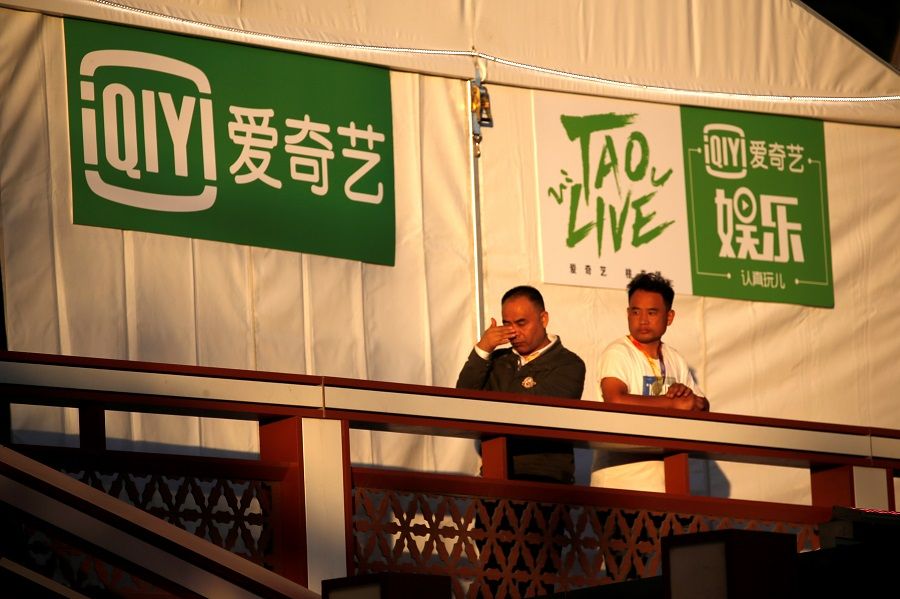 People stand near a booth with signs of iQiyi, during the Beijing International Film Festival, in Beijing, China, on 20 September 2021. (Tingshu Wang/Reuters)