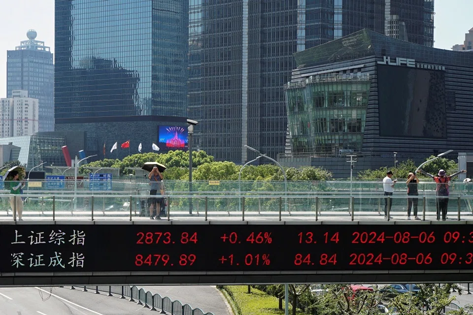 People on an overpass with a display of stock information in front of buildings in the Lujiazui financial district in Shanghai, China, on 6 August 2024. (Nicoco Chan/Reuters)