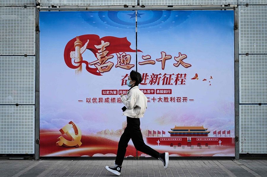 A woman walks past a propaganda poster welcoming the 20th Party Congress, along a street in Beijing, China, on 21 September 2022. (Jade Gao/AFP)
