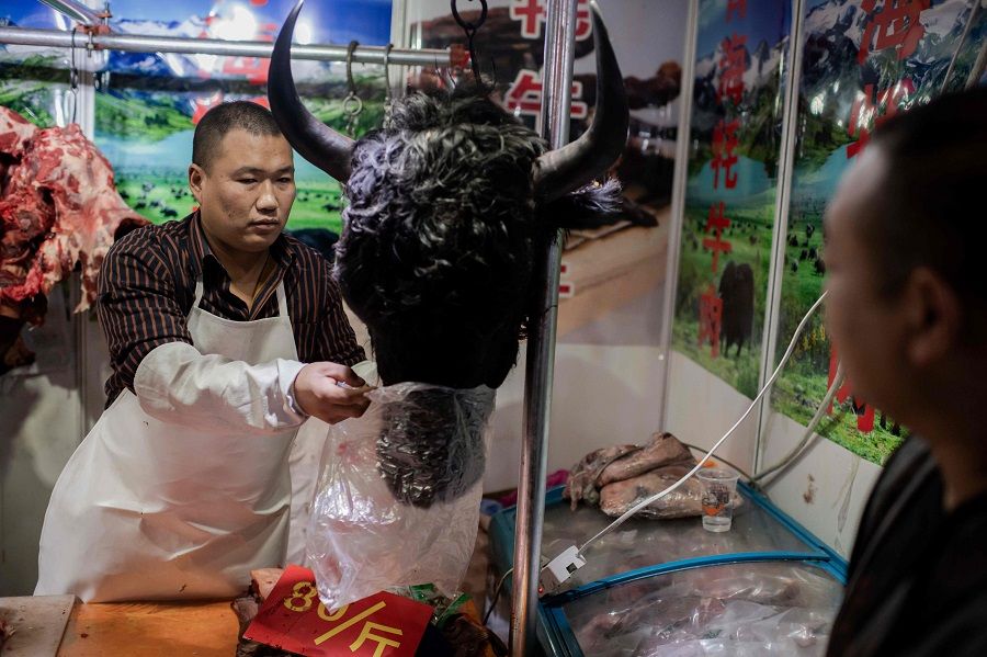 This picture taken on 15 January 2020 shows a butcher selling a yak's head to a customer at a market in Beijing. (Nicolas Asfouri/AFP)