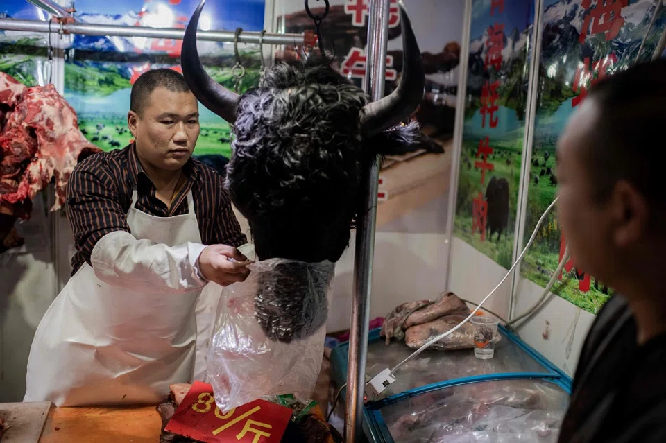 This picture taken on 15 January 2020 shows a butcher selling a yak's head to a customer at a market in Beijing. (Nicolas Asfouri/AFP)