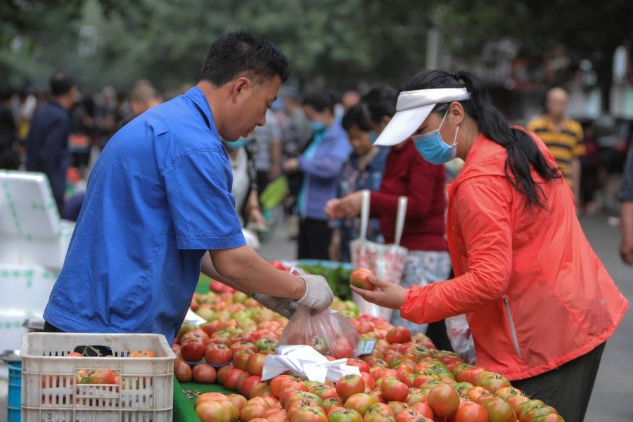 A customer (R) buys vegetables at an outdoor market in Shenyang in China's northeastern Liaoning province, 10 June 2020. (STR/AFP)