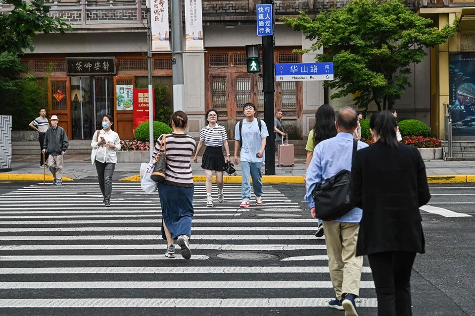 People cross a street at the Jing’an district in Shanghai on 31 May 2024.  (Hector Retamal/AFP)