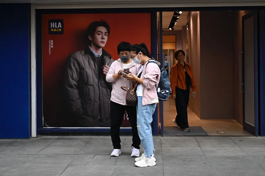 Women use their mobile phones outside a clothing shop in a shopping area in Beijing on 15 September 2025. (Wang Zhao/AFP)