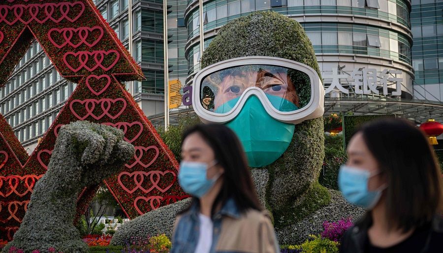 People wearing face masks walk past a flower display dedicated to frontline healthcare workers during the Covid-19 pandemic in celebration of the upcoming National Day of the People's Republic of China, in Beijing on 29 September 2020. (Nicolas Asfouri/AFP)