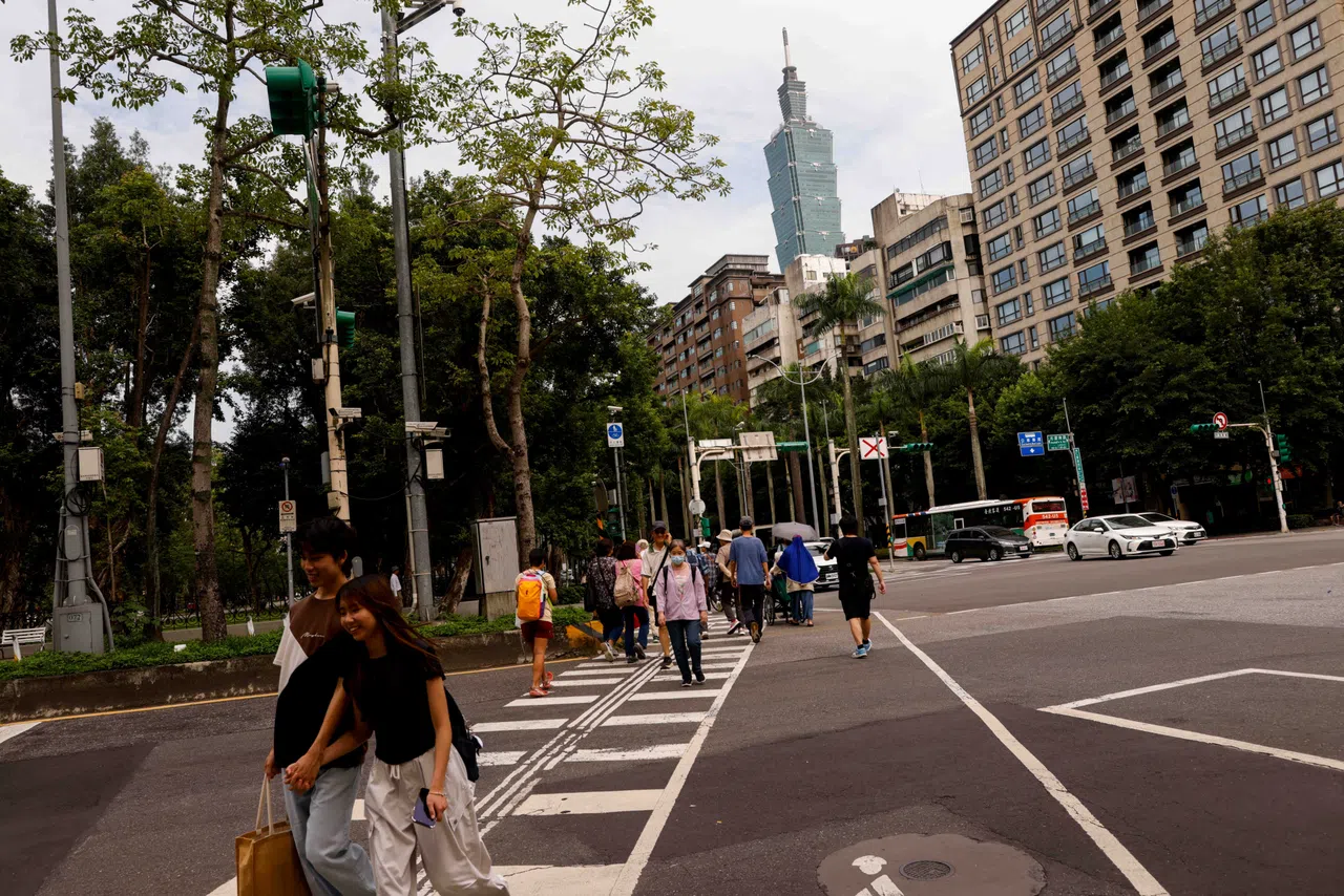 Taipei 101 rises in the background above residential buildings while people walk across a street in Taipei, Taiwan, on 12 May 2026.