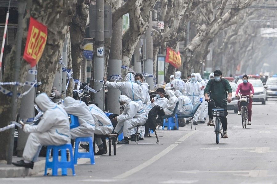 Workers are seen wearing protective clothes next to some lockdown areas after the detection of new cases of Covid-19 in Shanghai on 14 March 2022 (Hector Retamal/AFP)