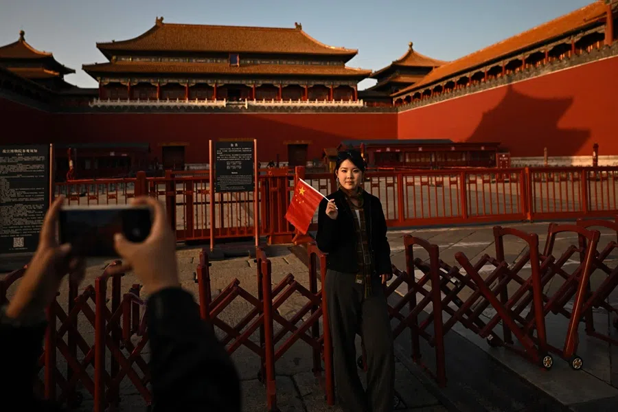 A woman holds a Chinese flag as she poses for a photo in front of the Forbidden City in Beijing during China's National Day Golden Week holiday on 6 October 2025.