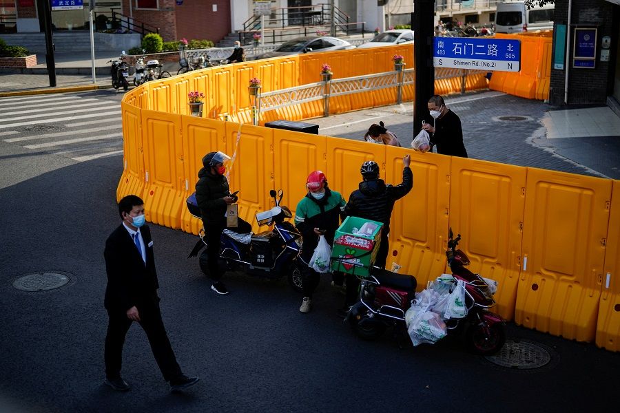 A delivery worker passes food to a man over the barriers of an area under lockdown amid the Covid-19 pandemic, in Shanghai, China, 23 March 2022. (Aly Song/Reuters)