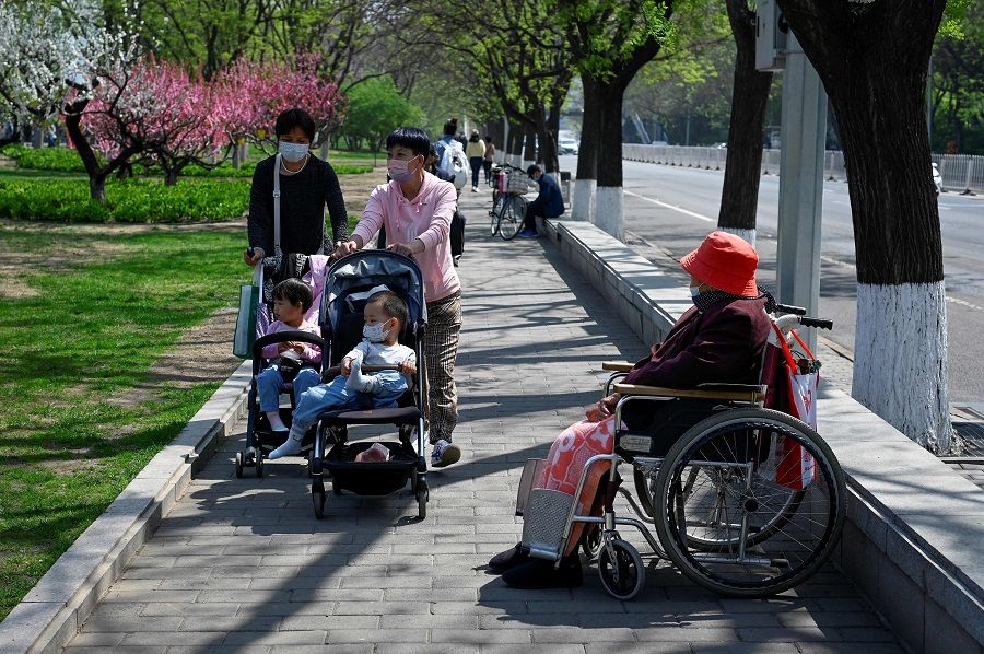 Two women push baby strollers past an elderly woman sitting in a wheelchair on a sidewalk in Beijing, China, on 19 April 2022. (Wang Zhao/AFP)