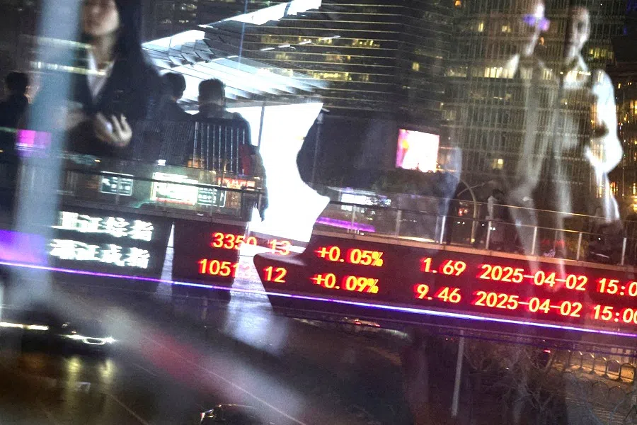 An electronic board shows Shanghai and Shenzhen stock indices as people walk on a pedestrian bridge at the Lujiazui financial district in Shanghai, China, on 2 April 2025.