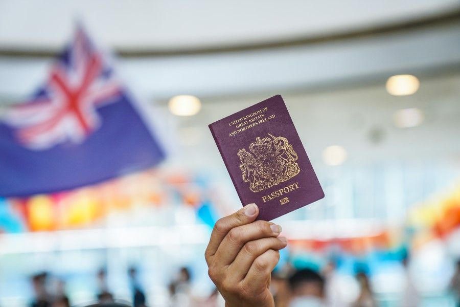 A demonstrator shows a British National (Overseas) passport as another waves a colonial-era Hong Kong flag during a lunchtime protest at the International Finance Center (IFC) shopping mall in Hong Kong, 29 May 2020. (Lam Yik/Bloomberg)