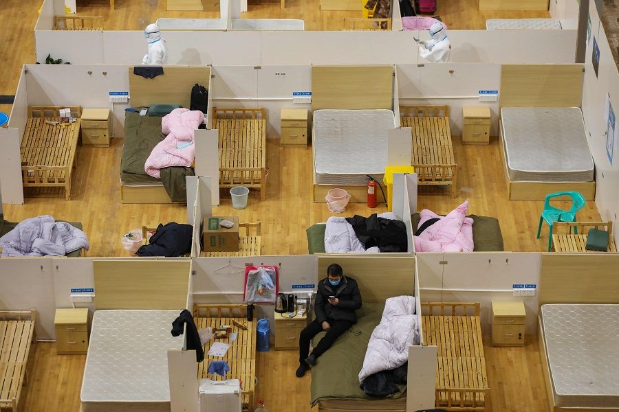 This photo taken on 5 March 2020 shows a medical worker (top left) walking past empty beds as a patient rests at a temporary hospital set up for Covid-19 coronavirus patients in a sports stadium in Wuhan. (STR/AFP)